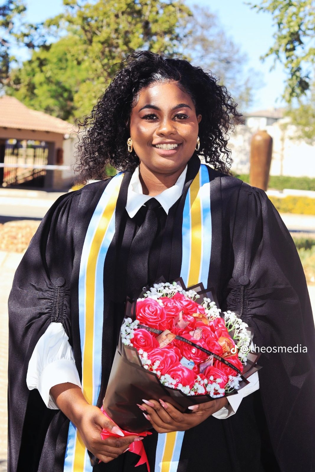 A graduate in a black gown holding a bouquet of red flowers