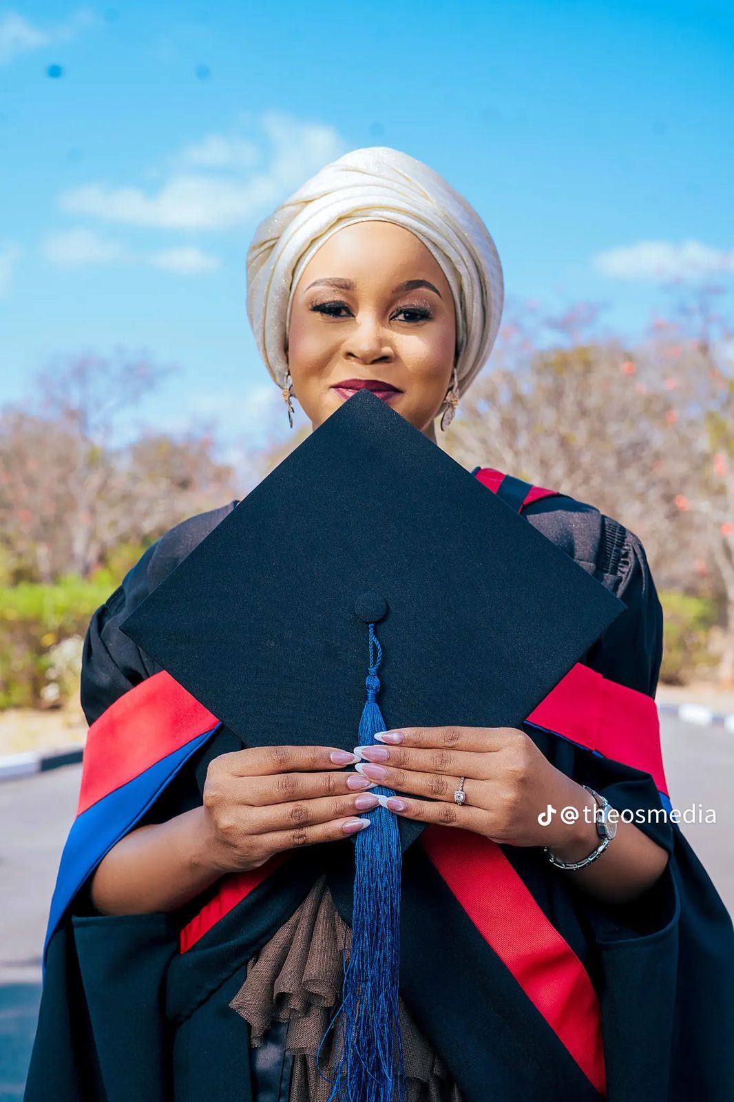 A graduate holding a black cap with a blue tassel