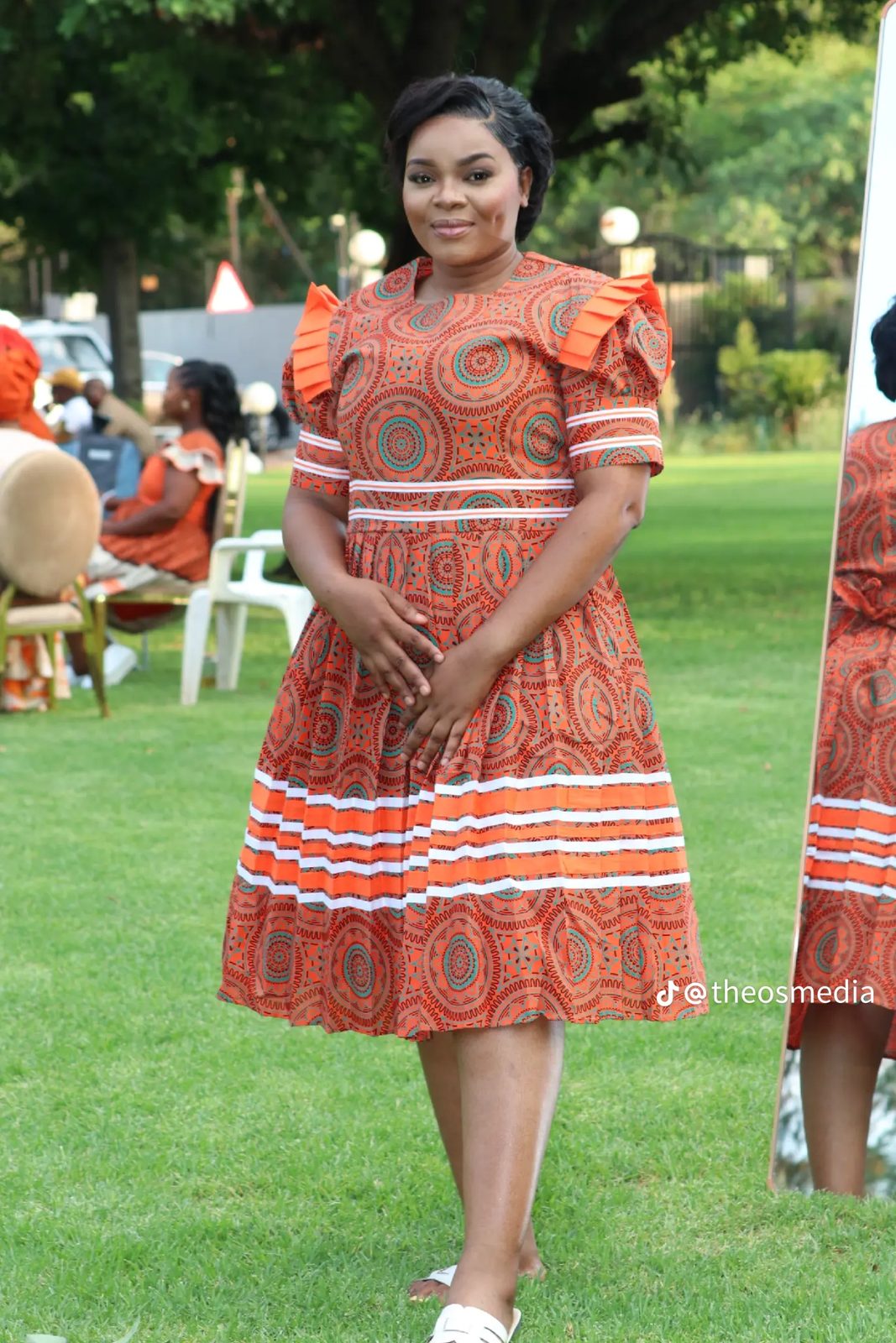A woman in an orange patterned dress standing on a lawn