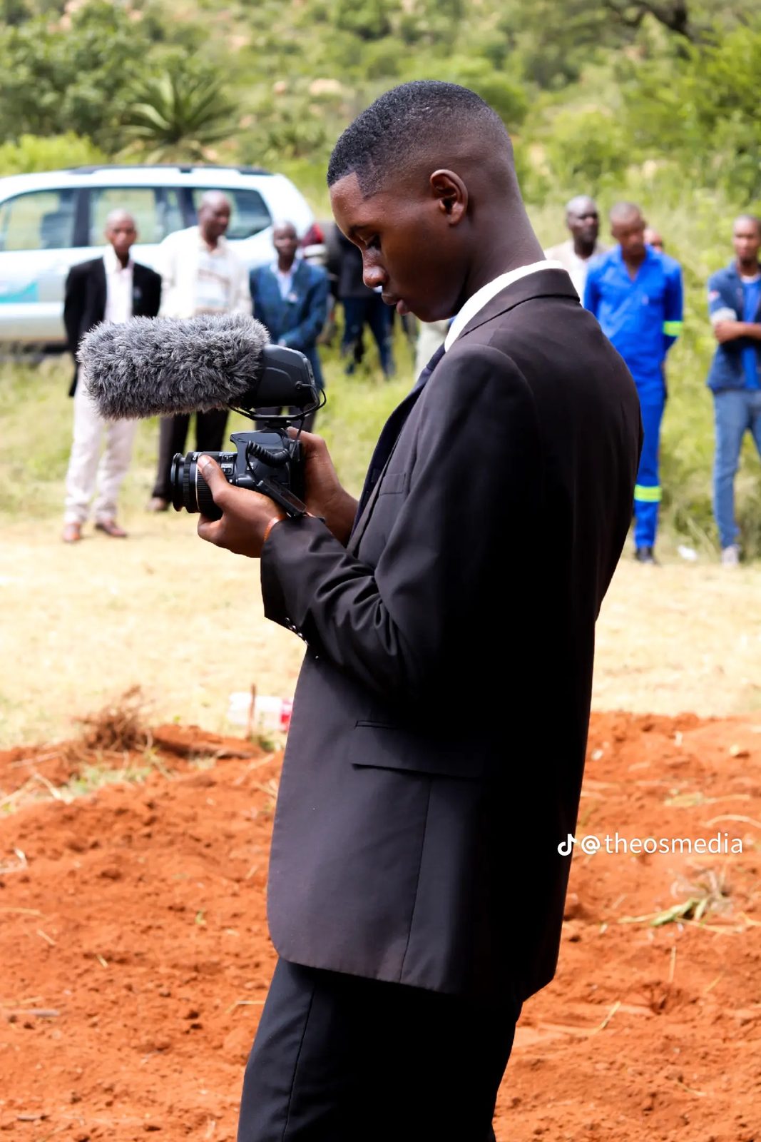A cameraman filming outdoors with a microphone on the camera