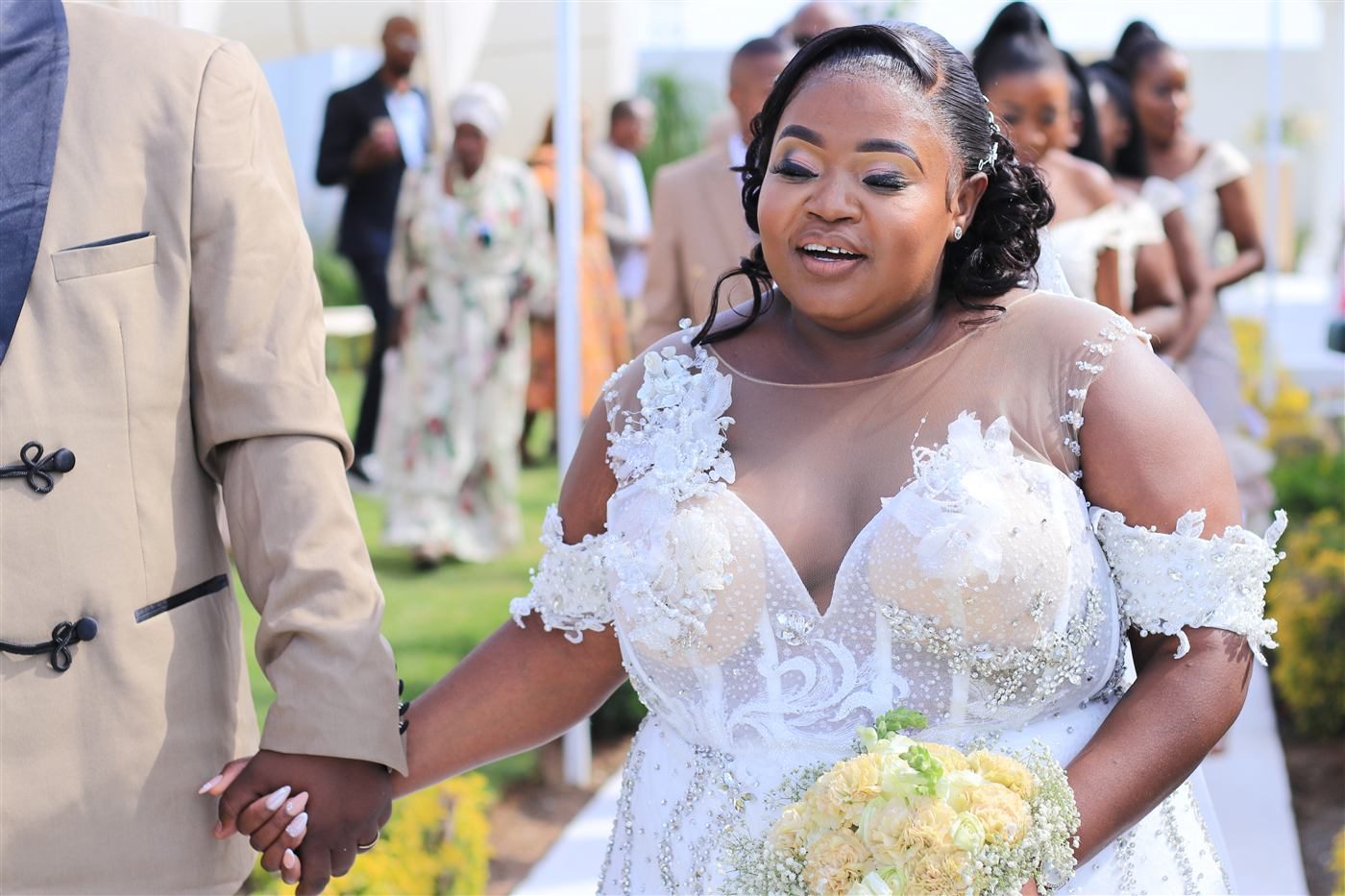 A bride in a beaded gown walking with the groom at an outdoor wedding