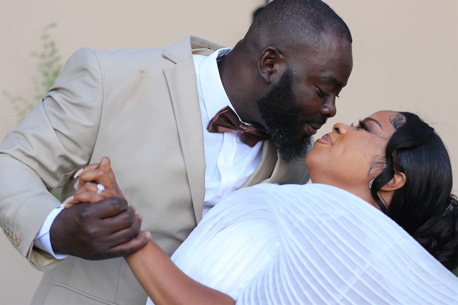 A couple in a close dance, the groom in a beige suit and the bride in a white pleated gown