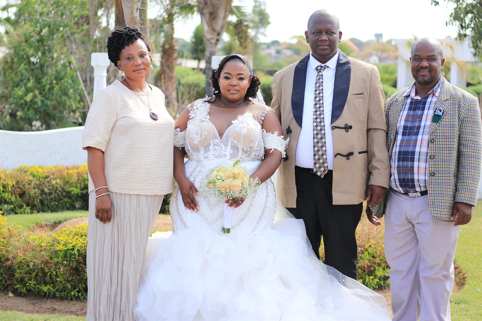 The bride and groom standing outdoors with two guests in the wedding garden