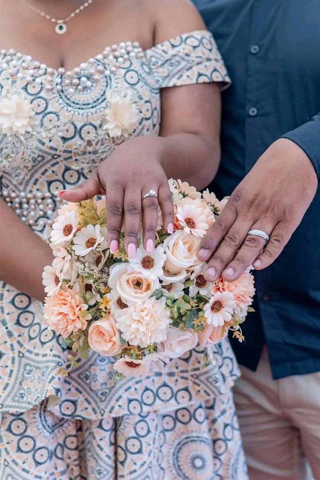 Close photograph of wedding rings and a bouquet held by the couple